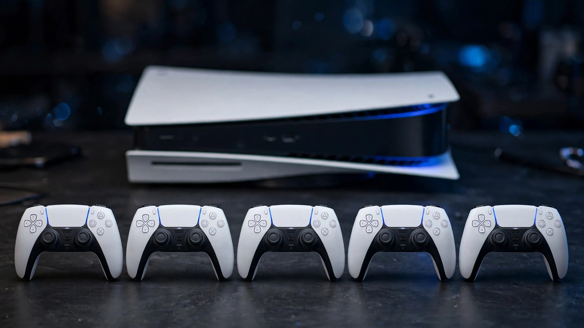 Five white PlayStation 5 controllers lined up in front of a PS5 console
